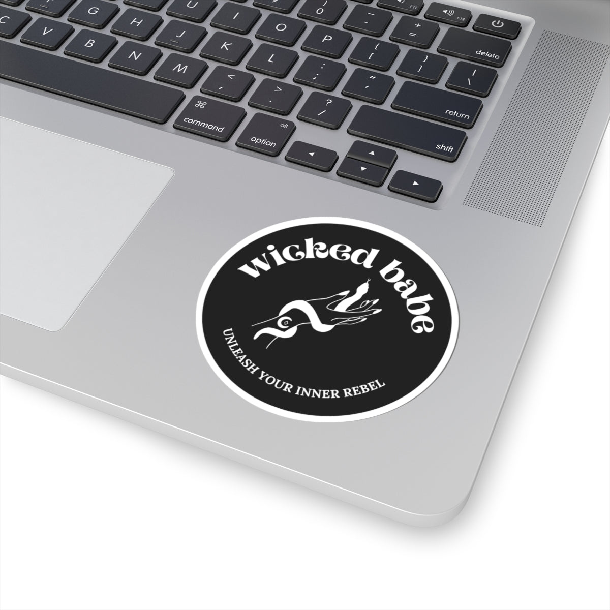 3 inch charcoal circular sticker with 'wicked babe' hand with serpent logo in white with a white border on a laptop