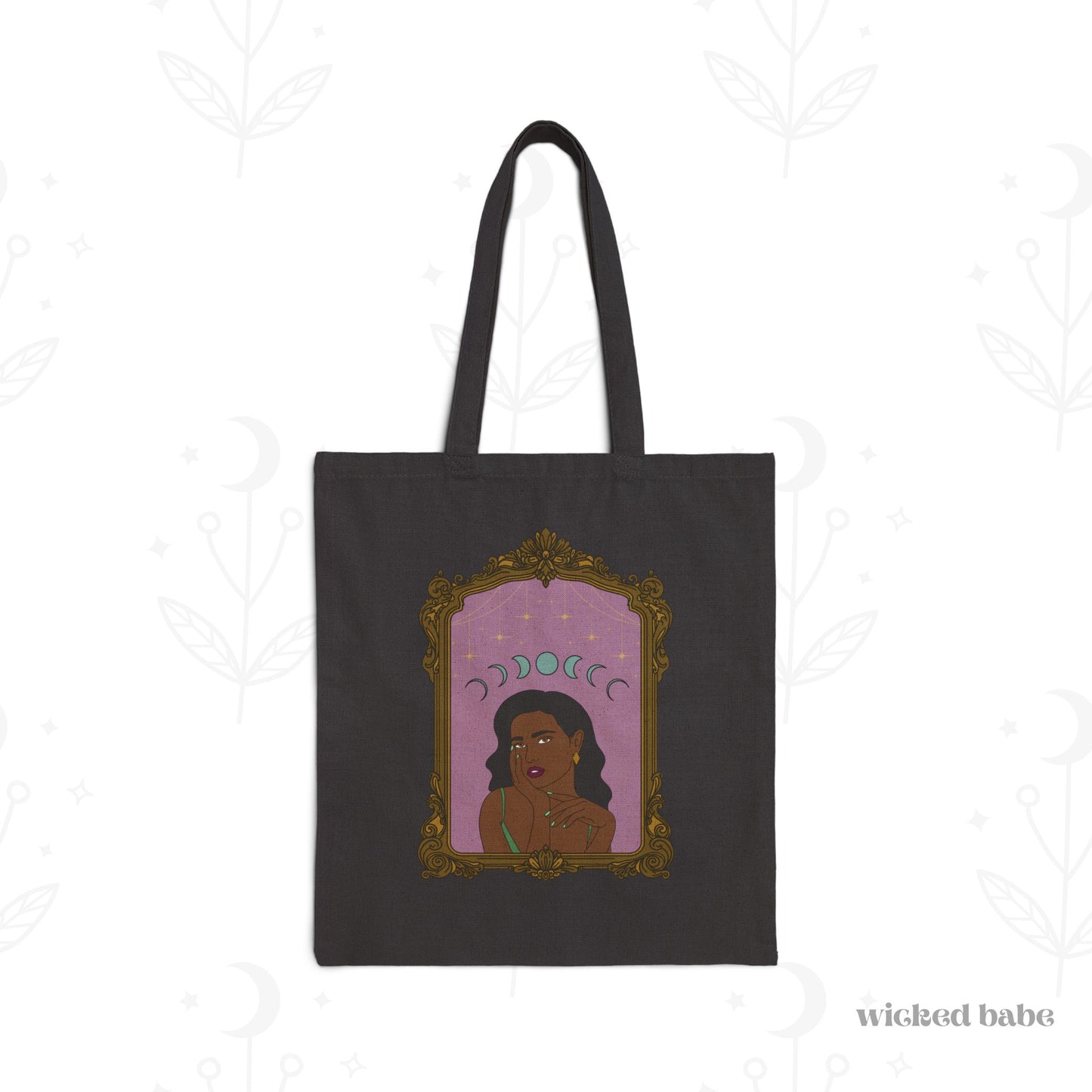 Black tote bag with design of a dark skinned woman with black hair wearing green on a pink background with moon phases above surrounded by ornate gold frame