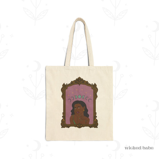 Canvas tote bag with design of a dark skinned woman with black hair wearing green on a pink background with moon phases above surrounded by ornate gold frame