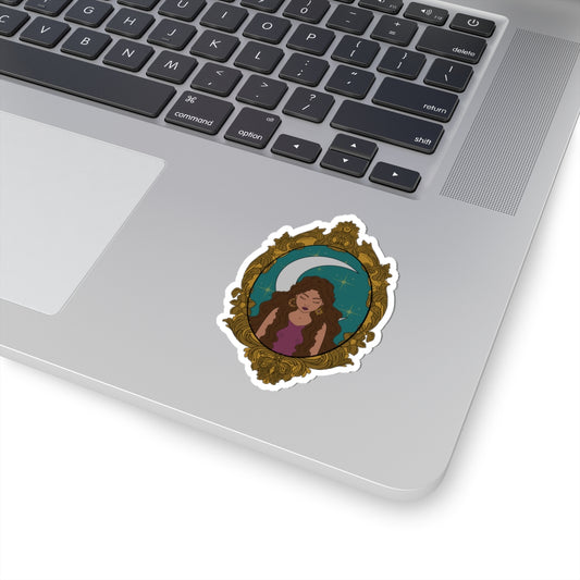 3 inch sticker with design of a tan skinned woman with brown wavy hair wearing purple in front of large crescent moon on a teal background surrounded by ornate gold frame with a white border on a laptop