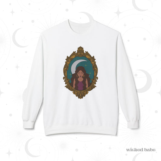 White long sleeve crewneck sweatshirt with design of a tan skinned woman with brown wavy hair wearing purple in front of large crescent moon on a teal background surrounded by ornate gold frame