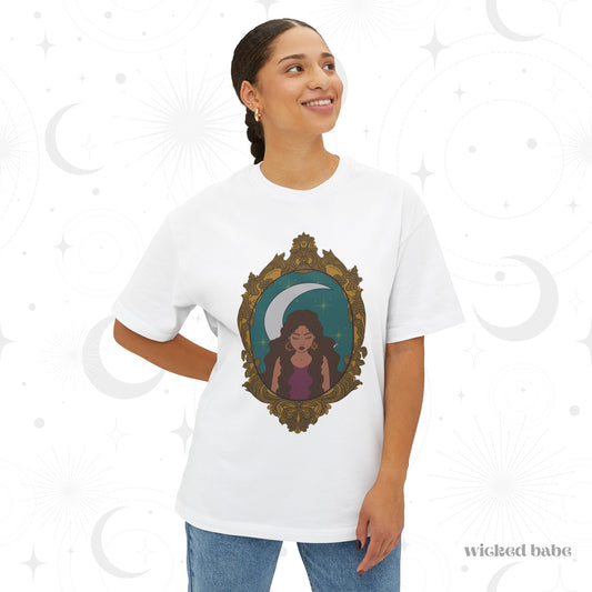 Woman wearing an oversized short sleeve white t-shirt with a design of a tan skinned woman with brown wavy hair wearing purple in front of large crescent moon on a teal background surrounded by ornate gold frame