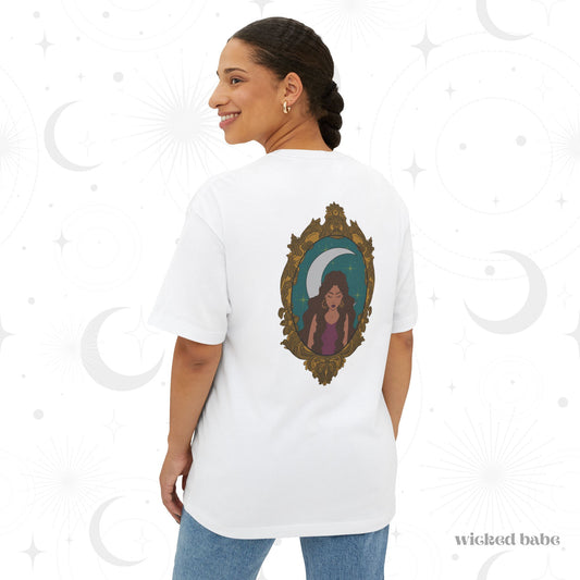 Woman wearing an oversized short sleeve white t-shirt with a design of a tan skinned woman with brown wavy hair wearing purple in front of large crescent moon on a teal background surrounded by ornate gold frame on the back