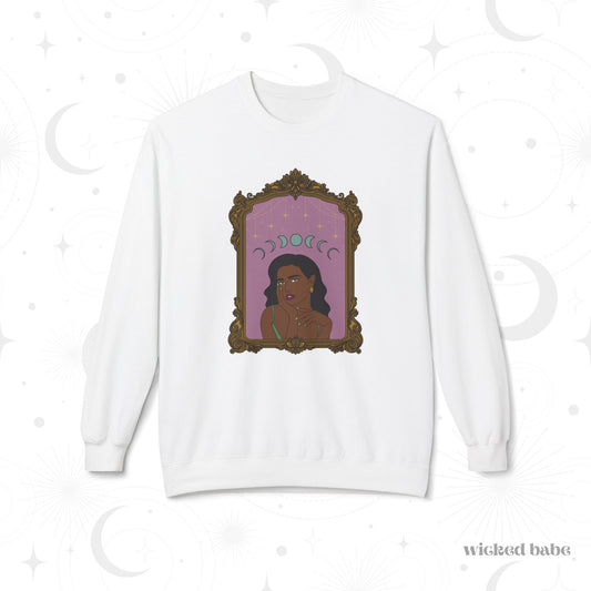 White long sleeve crewneck sweatshirt with design of a dark skinned woman with black hair wearing green on a pink background with moon phases above surrounded by ornate gold frame