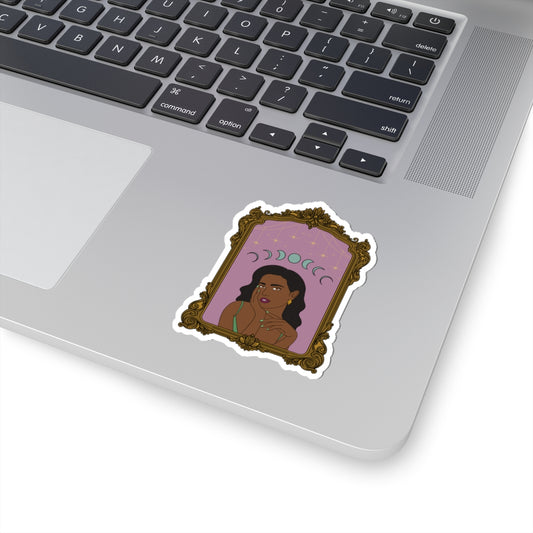 3 inch sticker with design of a dark skinned woman with black hair wearing green on a pink background with moon phases above surrounded by ornate gold frame with a white border on a laptop