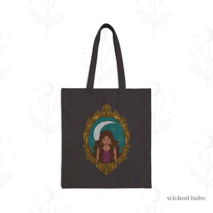 Black tote bag with design of a tan skinned woman with brown wavy hair wearing purple in front of large crescent moon on a teal background surrounded by ornate gold frame
