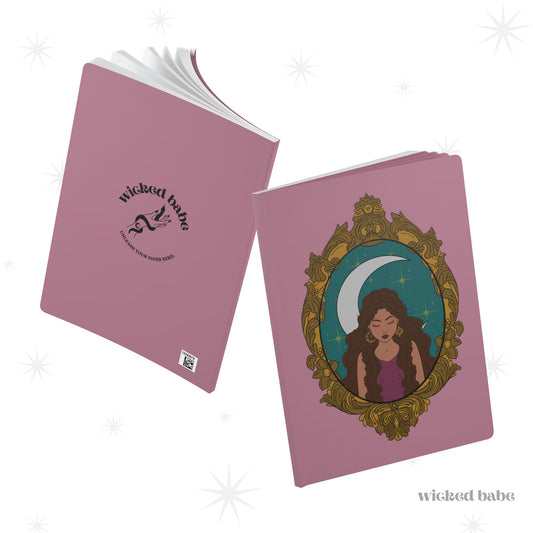 Front and back cover of pink softcover journal notebook with design of a tan skinned woman with brown wavy hair wearing purple in front of large crescent moon on a teal background surrounded by ornate gold frame on front and black wicked babe hand with serpent logo on back