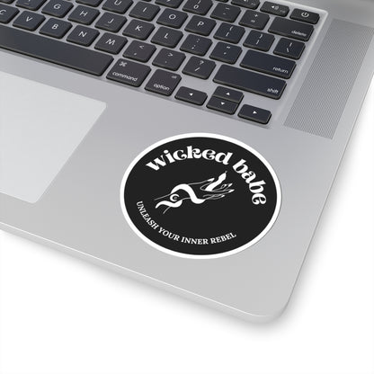 3 inch charcoal circular sticker with 'wicked babe' hand with serpent logo in white with a white border on a laptop