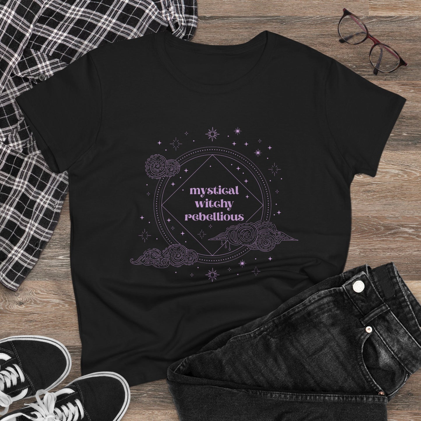 Black short sleeve crewneck t-shirt with mystical witchy rebellious text in purple surrounded by clouds and stars, on a wooden background with jeans and sneakers