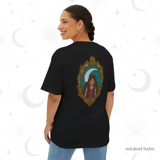 Woman wearing an oversized short sleeve black t-shirt with a design of a tan skinned woman with brown wavy hair wearing purple in front of large crescent moon on a teal background surrounded by ornate gold frame on the back