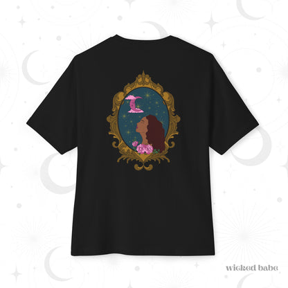 Oversized short sleeve black t-shirt with a design of a tan skinned woman with red brown wavy hair with pink flowers and a pink crescent moon above on a teal background surrounded by an ornate gold frame on the back
