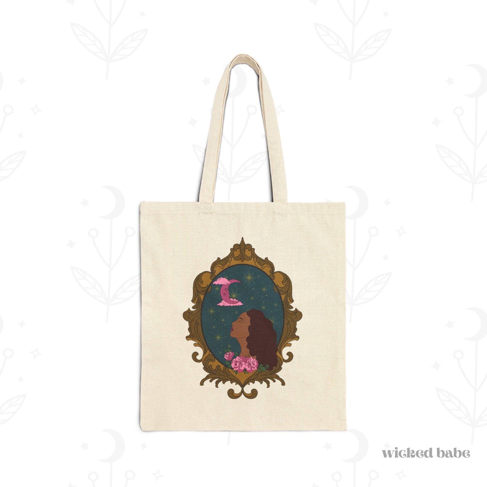 Canvas tote bag with design of a tan skinned woman with red brown wavy hair with pink flowers and a pink crescent moon above on a teal background surrounded by an ornate gold frame
