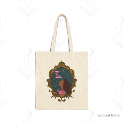 Canvas tote bag with design of a tan skinned woman with red brown wavy hair with pink flowers and a pink crescent moon above on a teal background surrounded by an ornate gold frame