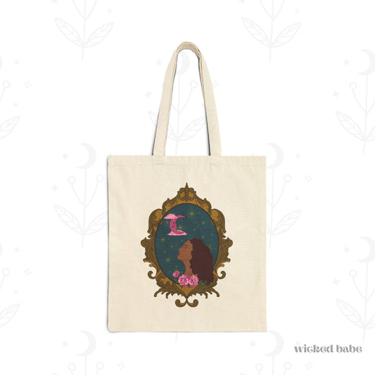 Canvas tote bag with design of a tan skinned woman with red brown wavy hair with pink flowers and a pink crescent moon above on a teal background surrounded by an ornate gold frame