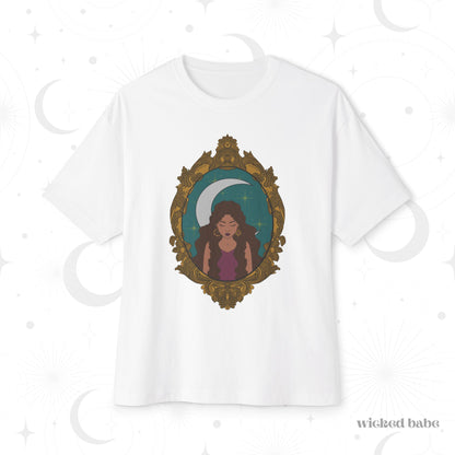 Oversized short sleeve white t-shirt with a design of a tan skinned woman with brown wavy hair wearing purple in front of large crescent moon on a teal background surrounded by ornate gold frame