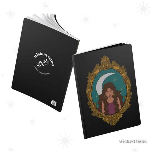 Front and back cover of black softcover journal notebook with design of a tan skinned woman with brown wavy hair wearing purple in front of large crescent moon on a teal background surrounded by ornate gold frame on front and white wicked babe hand with serpent logo in the center on the back