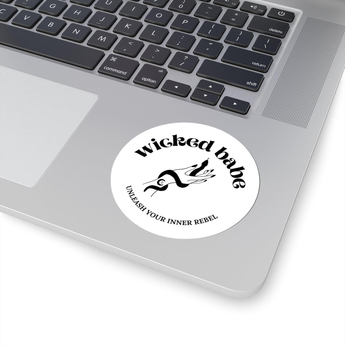 3 inch white circular sticker with 'wicked babe' hand with serpent logo in black on a laptop