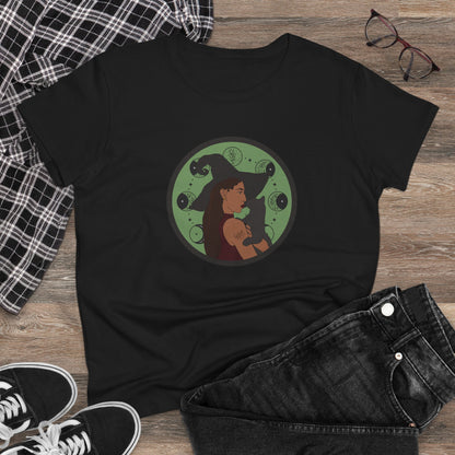 Black short sleeve crew neck t-shirt featuring a design of a woman wearing a witch's hat holding a gray cat with moon phases on a green background, displayed as a flatlay with jeans and sneakers