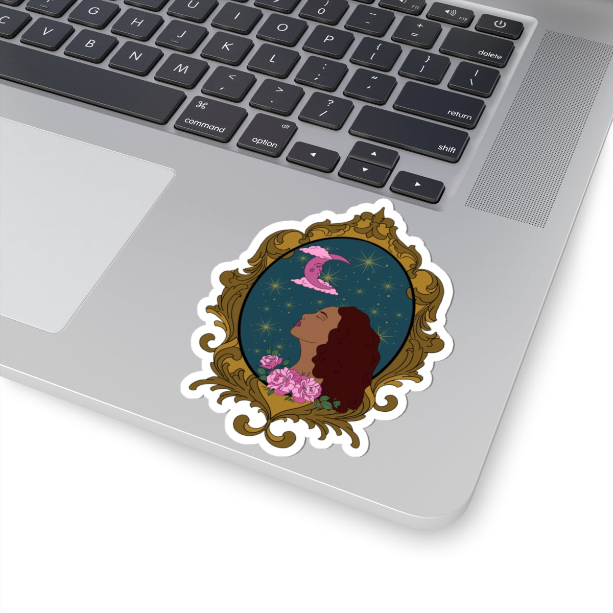 4 inch sticker with design of a tan skinned woman with red brown wavy hair with pink flowers and a pink crescent moon above on a teal background surrounded by an ornate gold frame with a white border on a laptop