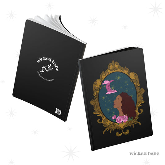 Front and back cover of black softcover journal notebook with design of a tan skinned woman with red brown wavy hair with pink flowers and a pink crescent moon above on a teal background surrounded by an ornate gold frame on front and white wicked babe hand with serpent logo on back