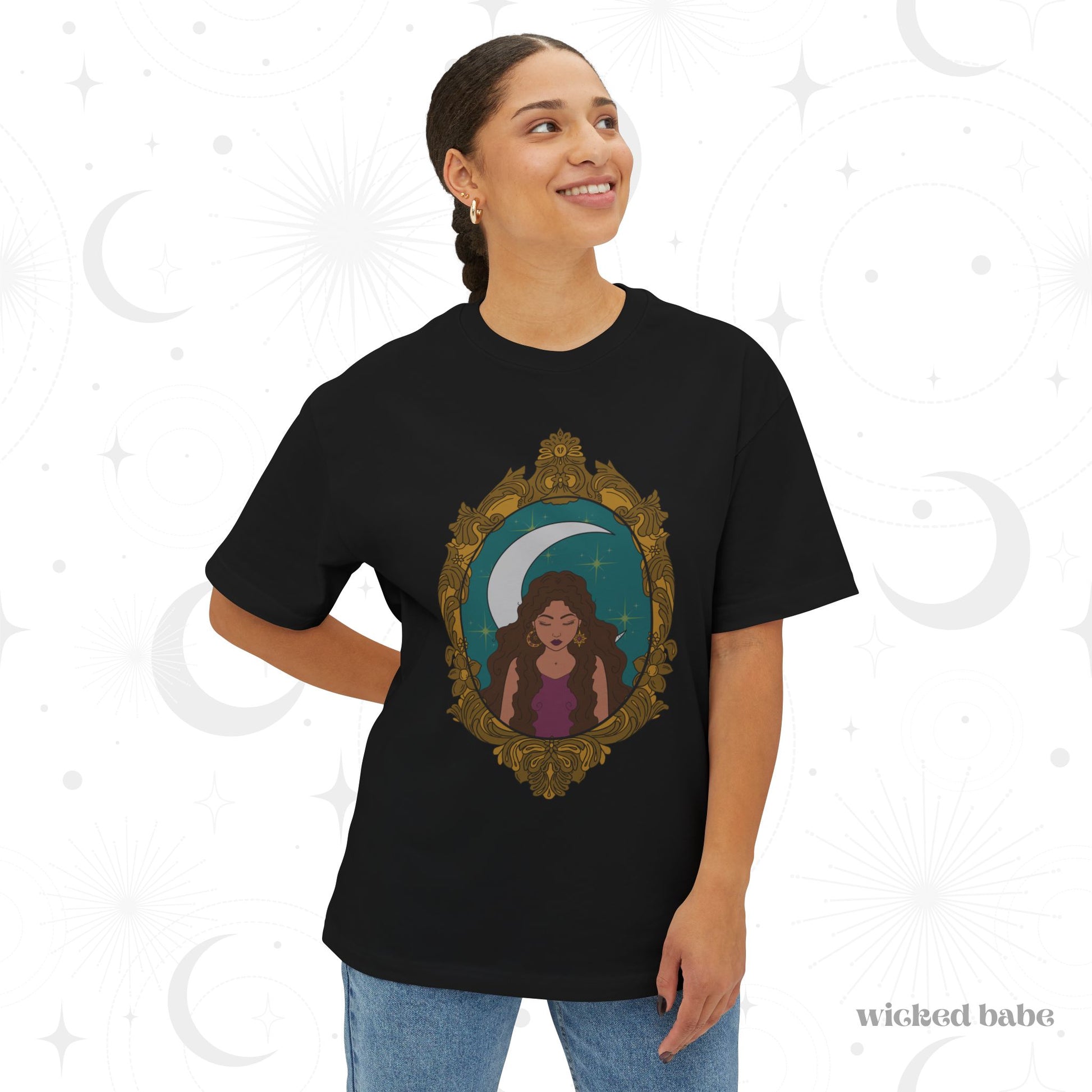 Woman wearing an oversized short sleeve black t-shirt with a design of a tan skinned woman with brown wavy hair wearing purple in front of large crescent moon on a teal background surrounded by ornate gold frame