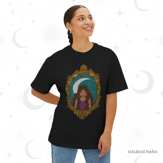 Woman wearing an oversized short sleeve black t-shirt with a design of a tan skinned woman with brown wavy hair wearing purple in front of large crescent moon on a teal background surrounded by ornate gold frame
