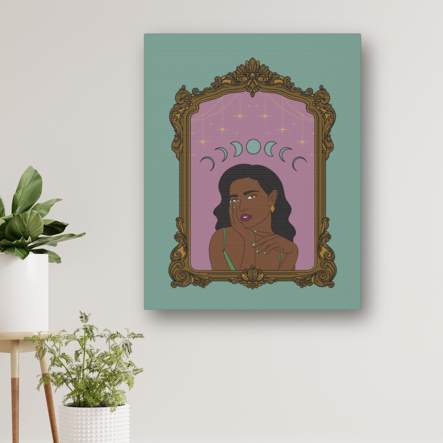 Matte green canvas wall art with design of a dark skinned woman with black hair wearing green on a pink background with moon phases above surrounded by ornate gold frame hung on a wall near plants