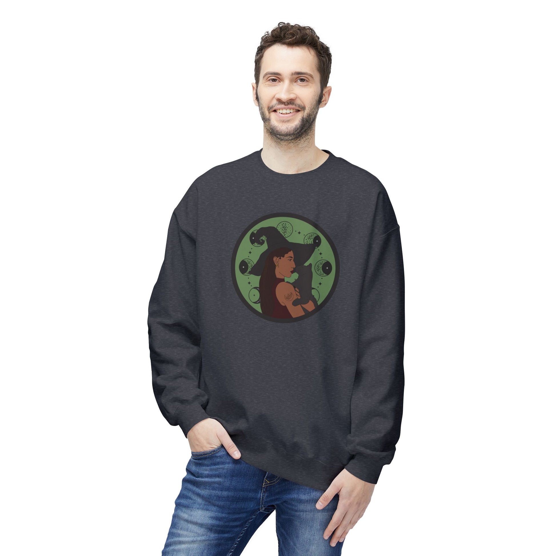 Man wearing a dark heather gray crewneck long sleeve pullover sweatshirt featuring a design of a woman wearing a witch's hat holding a gray cat with moon phases on a green background