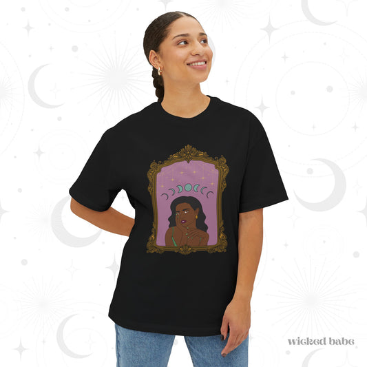 Woman wearing an oversized short sleeve black t-shirt with design of a dark skinned woman with black hair wearing green on a pink background with moon phases above surrounded by ornate gold frame