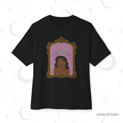 Oversized short sleeve black t-shirt with design of a dark skinned woman with black hair wearing green on a pink background with moon phases above surrounded by ornate gold frame
