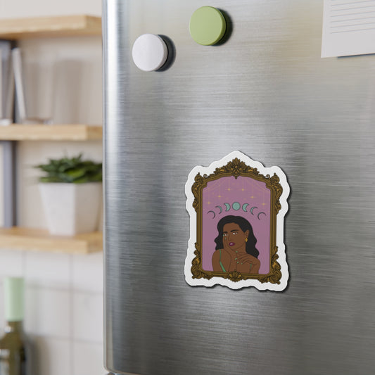 Refrigerator magnet with design of a dark skinned woman with black hair wearing green on a pink background with moon phases above surrounded by ornate gold frame with a white border on a stainless steel fridge