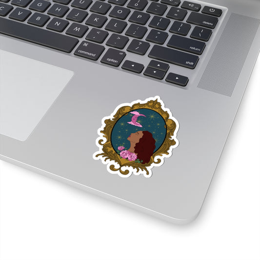 3 inch sticker with design of a tan skinned woman with red brown wavy hair with pink flowers and a pink crescent moon above on a teal background surrounded by an ornate gold frame with a white border on a laptop