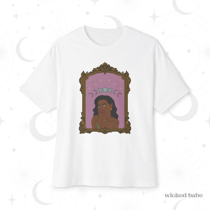 Oversized short sleeve white t-shirt with design of a dark skinned woman with black hair wearing green on a pink background with moon phases above surrounded by ornate gold frame