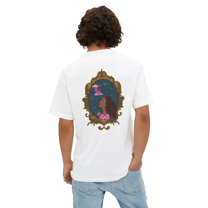 Man wearing an oversized short sleeve white t-shirt with a ddesign of a tan skinned woman with red brown wavy hair with pink flowers and a pink crescent moon above on a teal background surrounded by an ornate gold frame on the back