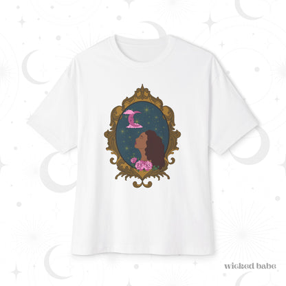 Oversized short sleeve white t-shirt with a design of a tan skinned woman with red brown wavy hair with pink flowers and a pink crescent moon above on a teal background surrounded by an ornate gold frame