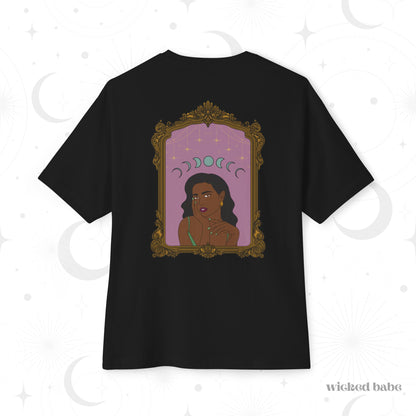 Oversized short sleeve black t-shirt with design of a dark skinned woman with black hair wearing green on a pink background with moon phases above surrounded by ornate gold frame on the back