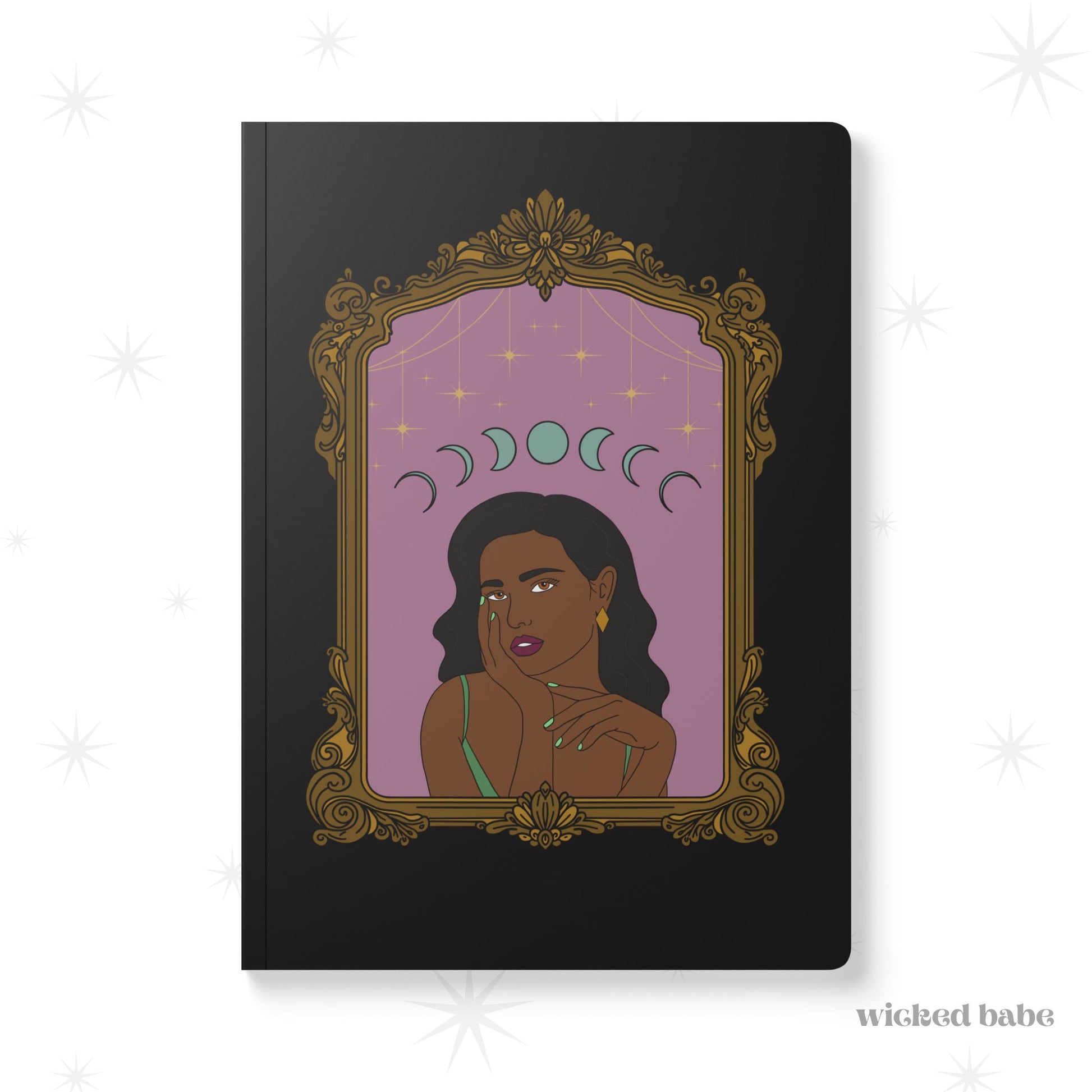 Front cover of black softcover journal notebook with design of a dark skinned woman with black hair wearing green on a pink background with moon phases above surrounded by ornate gold frame