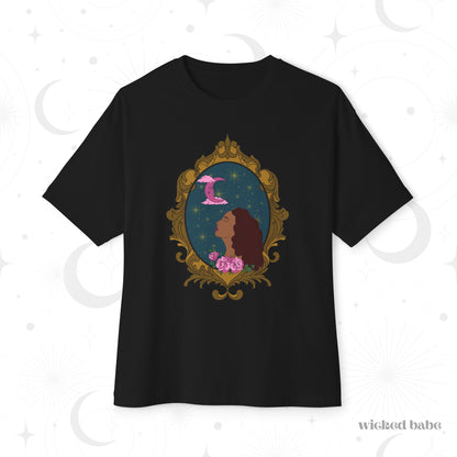 Oversized short sleeve black t-shirt with a design of a tan skinned woman with red brown wavy hair with pink flowers and a pink crescent moon above on a teal background surrounded by an ornate gold frame