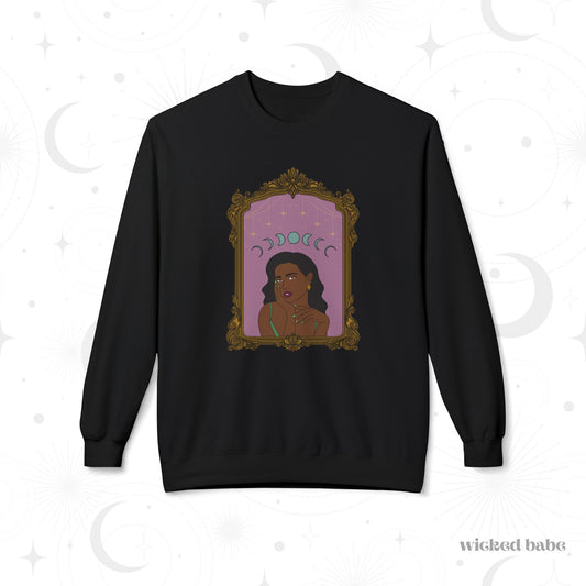 Black long sleeve crewneck sweatshirt with design of a dark skinned woman with black hair wearing green on a pink background with moon phases above surrounded by ornate gold frame