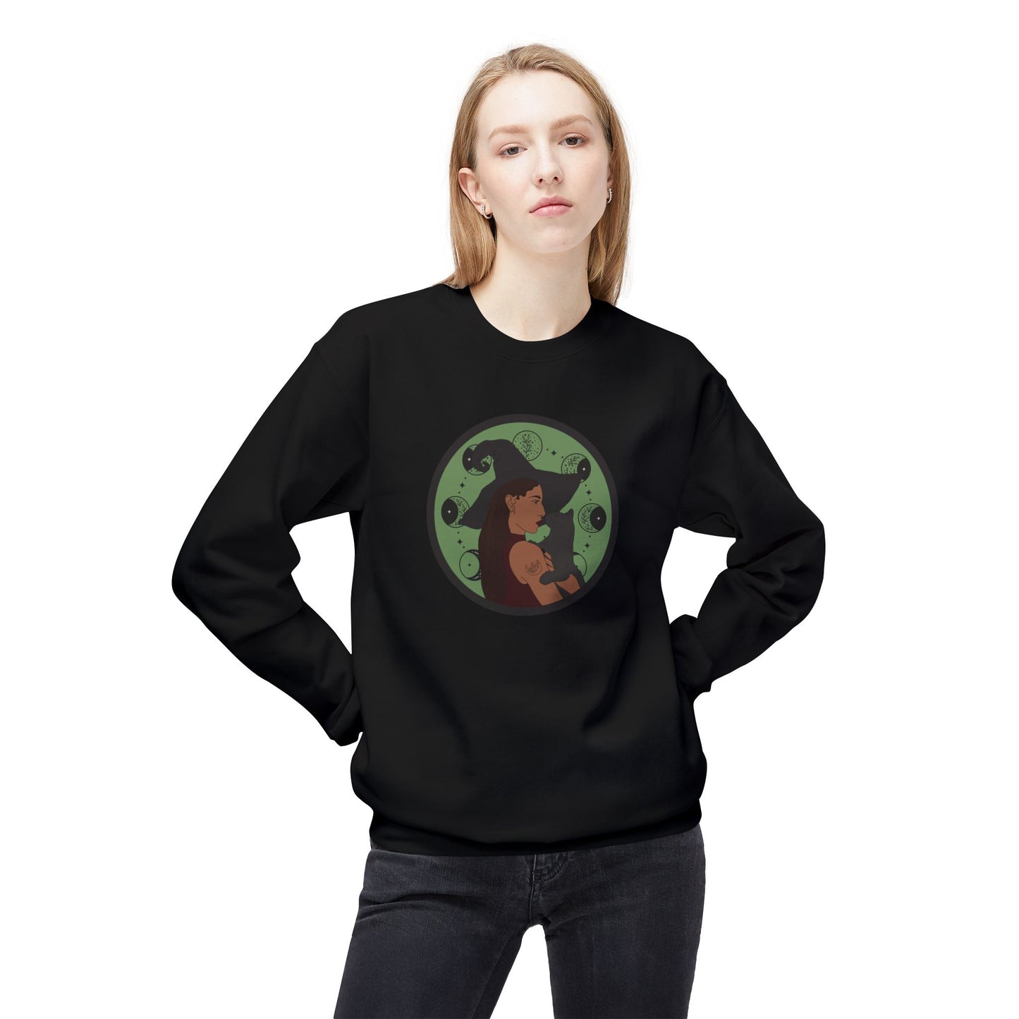 Woman wearing a black crewneck long sleeve pullover sweatshirt featuring a design of a woman wearing a witch's hat holding a gray cat with moon phases on a green background